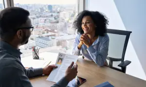 Entrevista de trabajo. Un hombre revisa un CV mientras una mujer sonríe, discutiendo sus debilidades para una entrevista.