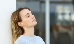 Mujer con ojos cerrados, apoyada en pared blanca, reflexionando sobre cuanto se cobra estando de baja por ansiedad.