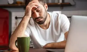 Hombre con dolor de cabeza frente a un portátil, con una taza verde. Necesita un justificante médico Andalucía.