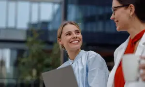 Jóvenes profesionales sonríen y colaboran con un portátil, disfrutando de la flexibilidad horaria en un entorno moderno.