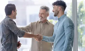 Tres hombres sonríen y se dan la mano, un ejemplo de inteligencia emocional en la empresa.