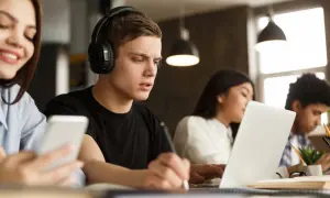 Estudiantes concentrados, uno con auriculares y portátil, aprendiendo cómo homologar un curso privado.