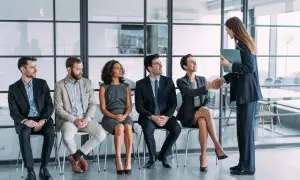 Un grupo de personas espera en fila para una entrevista de trabajo. Una mujer sonríe mientras le da la mano a otra mujer, quizás sintiendo que no me adapto a mi nuevo trabajo.