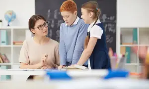 Profesora explica a dos niños. Ella se prepara para preparar oposiciones educación infantil, inspirando a sus alumnos.