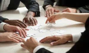 Manos diversas unen piezas de un rompecabezas, simulando una dinámica isla desierta donde la colaboración es clave para el éxito.