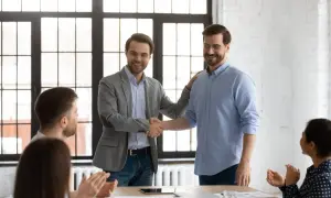 Dos hombres se dan la mano en una oficina, celebrando el fin del periodo de prueba en contratos temporales.