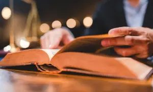 Man reading a thick book, a symbol of justice in the background. A visual guide on como estudiar leyes.