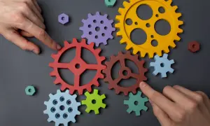 Manos ensamblan engranajes de colores, demostrando la capacidad de adaptación para crear un sistema funcional.