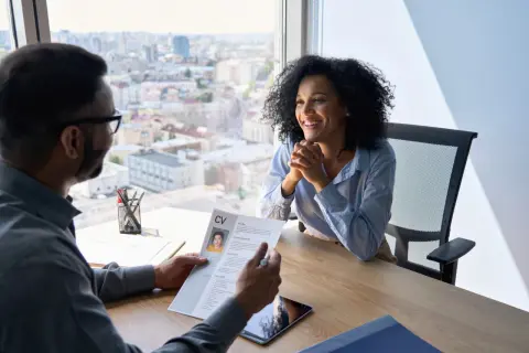 Entrevista de trabajo. Un hombre revisa un CV mientras una mujer sonríe, discutiendo sus debilidades para una entrevista.
