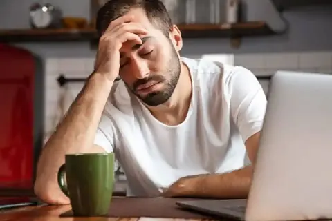 Hombre con dolor de cabeza frente a un portátil, con una taza verde. Necesita un justificante médico Andalucía.
