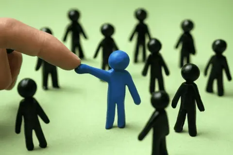 Dedo señala a figura azul entre otras negras, sugiriendo la necesidad de denunciar favoritismo laboral.