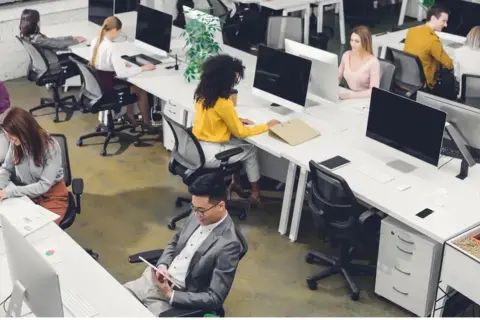 Personas trabajando en oficinas modernas, ejemplos de trabajos sedentarios.