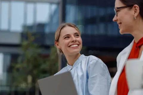 Jóvenes profesionales sonríen y colaboran con un portátil, disfrutando de la flexibilidad horaria en un entorno moderno.