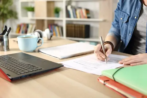 Persona concentrada en la tramitación procesal de un concurso oposición, escribiendo en documentos.