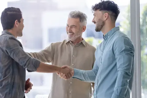 Tres hombres sonríen y se dan la mano, un ejemplo de inteligencia emocional en la empresa.