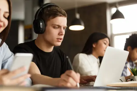 Estudiantes concentrados, uno con auriculares y portátil, aprendiendo cómo homologar un curso privado.