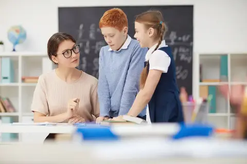 Profesora explica a dos niños. Ella se prepara para preparar oposiciones educación infantil, inspirando a sus alumnos.