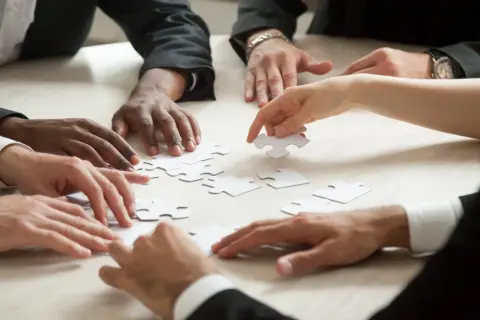 Manos diversas unen piezas de un rompecabezas, simulando una dinámica isla desierta donde la colaboración es clave para el éxito.