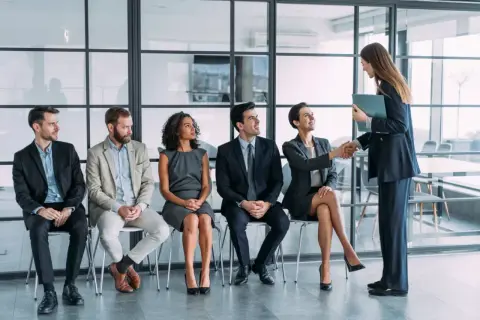 Candidatos esperan su turno para una entrevista de trabajo. Una mujer saluda a otra, un paso clave en la adaptacion laboral.