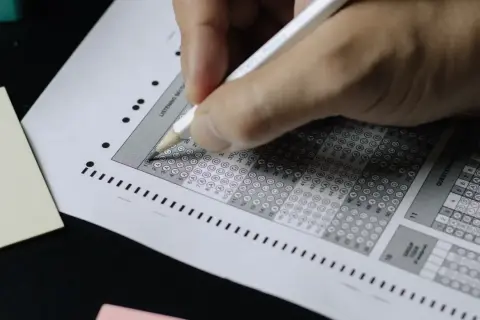 Mano completando una hoja de respuestas tipo test. ¡Descubre trucos para aprobar oposiciones tipo test y domina el examen!