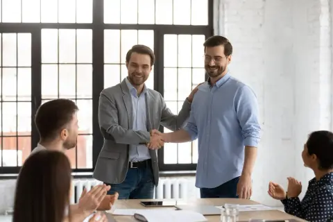 Dos hombres se dan la mano en una oficina, celebrando el fin del periodo de prueba en contratos temporales.
