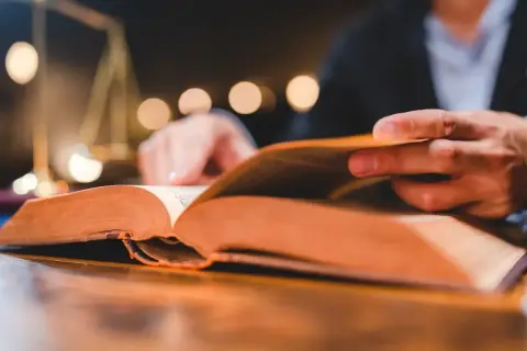 Man reading a thick book, a symbol of justice in the background. A visual guide on como estudiar leyes.