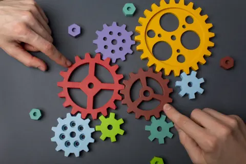 Manos ensamblan engranajes de colores, demostrando la capacidad de adaptación para crear un sistema funcional.