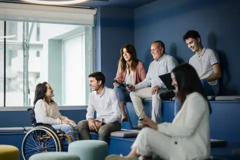 Un equipo diverso colabora en una **empresa social**. Una mujer en silla de ruedas sonríe a un colega.
