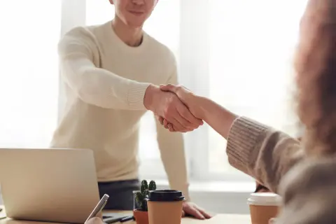 Dos personas se dan la mano, un gesto que demuestra confianza y respeto, aplicando técnicas de asertividad en un entorno de oficina.