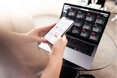 Manos organizando calendarios en un teléfono y portátil. Planificar bien para que los días de reposo se pagan.
