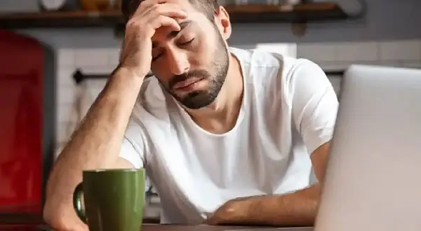 Hombre con dolor de cabeza frente a un portátil, con una taza verde. Necesita un justificante médico Andalucía.