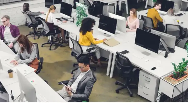 Personas trabajando en oficinas modernas, ejemplos de trabajos sedentarios.