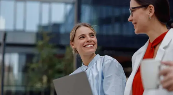 Jóvenes profesionales sonríen y colaboran con un portátil, disfrutando de la flexibilidad horaria en un entorno moderno.