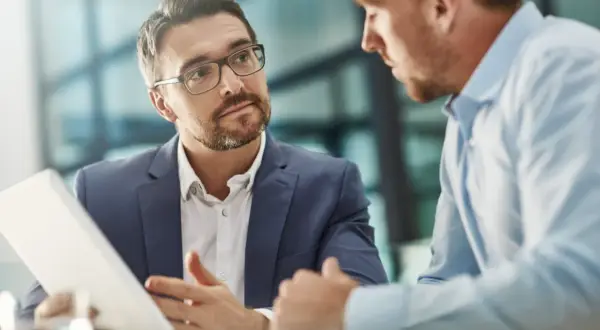 Un consultor de RRHH con gafas explica algo en una tablet a un colega.