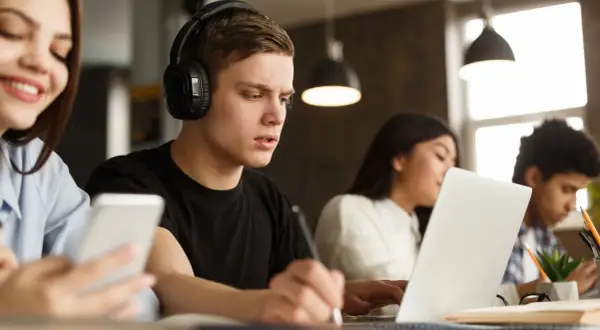 Estudiantes concentrados, uno con auriculares y portátil, aprendiendo cómo homologar un curso privado.