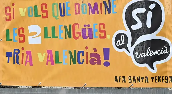Cartel naranja con letras de colores: "Si vols que domines les llengües, tria València!". Promociona cursos homologados en València.