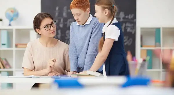 Profesora explica a dos niños. Ella se prepara para preparar oposiciones educación infantil, inspirando a sus alumnos.