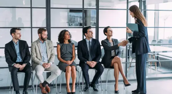 Candidatos esperan su turno para una entrevista de trabajo. Una mujer saluda a otra, un paso clave en la adaptacion laboral.