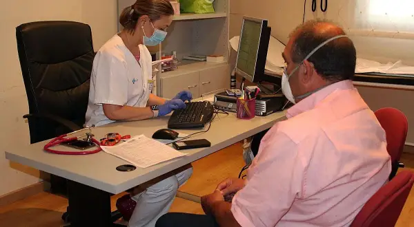 Enfermera con mascarilla atiende a paciente con mascarilla, tramitando un hospital justificante médico urgencias.