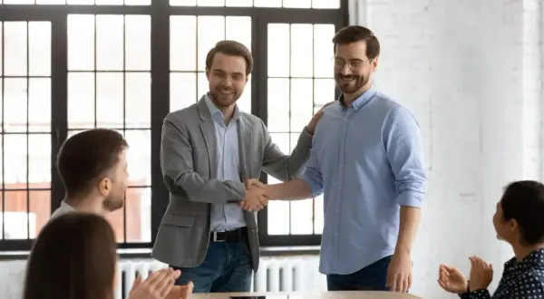 Dos hombres se dan la mano en una oficina, celebrando el fin del periodo de prueba en contratos temporales.