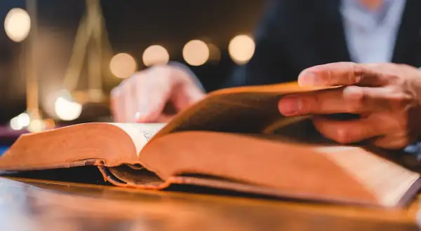 Man reading a thick book, a symbol of justice in the background. A visual guide on como estudiar leyes.