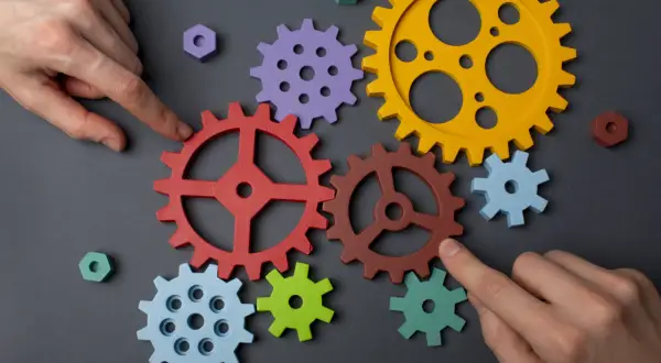 Manos ensamblan engranajes de colores, demostrando la capacidad de adaptación para crear un sistema funcional.