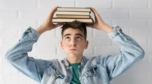 Joven con libros en la cabeza, pensando en la probabilidad de aprobar oposiciones a la primera.