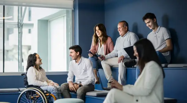 Un equipo diverso colabora en una **empresa social**. Una mujer en silla de ruedas sonríe a un colega.