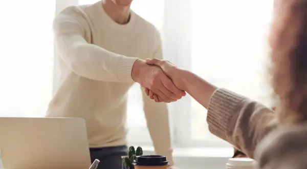 Dos personas se dan la mano, un gesto que demuestra confianza y respeto, aplicando técnicas de asertividad en un entorno de oficina.