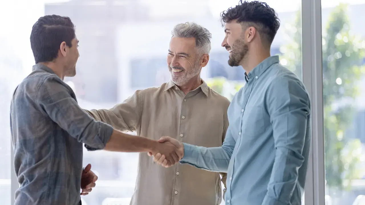 Tres hombres sonríen y se dan la mano, un ejemplo de inteligencia emocional en la empresa.