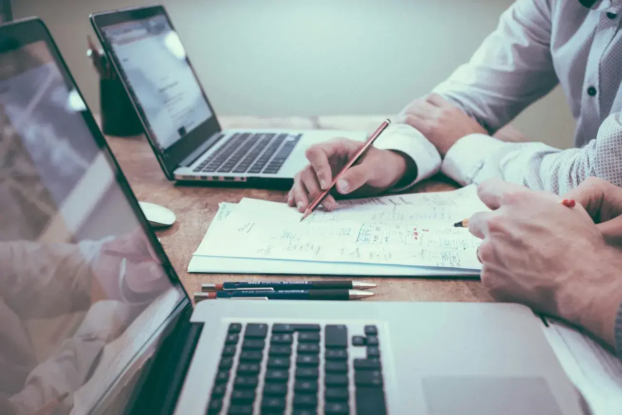 Dos personas analizan documentos y planifican, quizás sobre una nomina retribucion flexible. Laptops y bolígrafos a la vista.