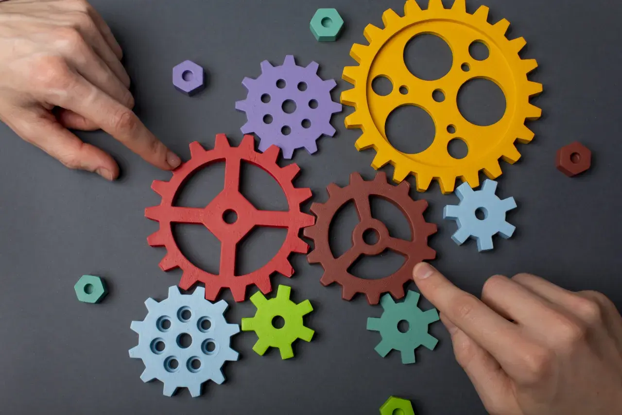 Manos ensamblan engranajes de colores, demostrando la capacidad de adaptación para crear un sistema funcional.