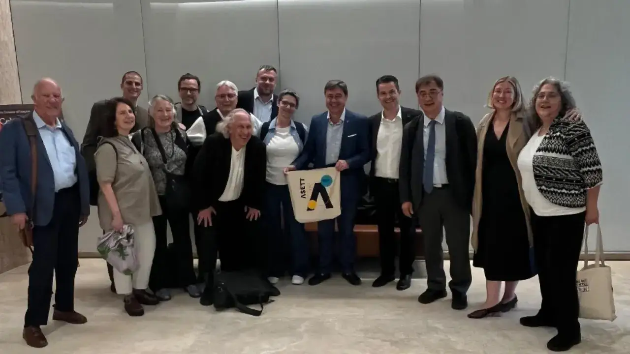 Grupo diverso posa para foto, algunos con bolsa de ASETT, representando una empresa social comprometida.