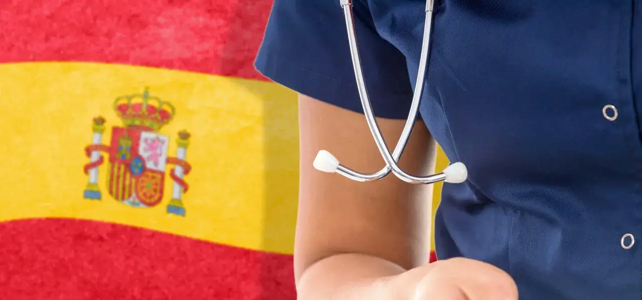 Un profesional de la salud con un estetoscopio frente a la bandera de España. En España, los días de reposo se pagan.